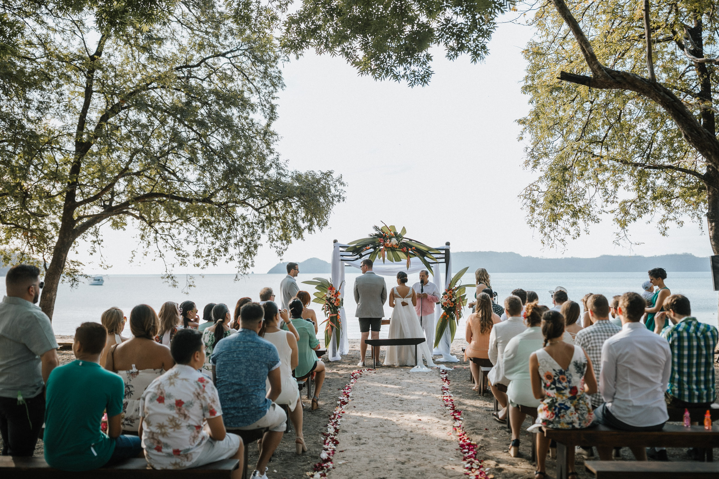 Heiraten in Costa Rica - Brautpaar steht am Altar, Aufnahme der Strandhochzeits-gesellschaft von hinten 