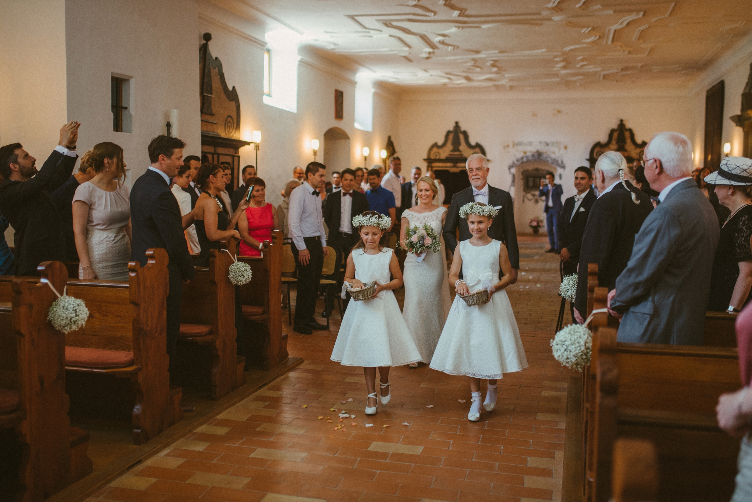 Hochzeit in der Schweiz: Braut und Brautvater laufen durch den Kirchgang, alle Gäste stehen links und rechts, im Vordergrund Blumenmädchen