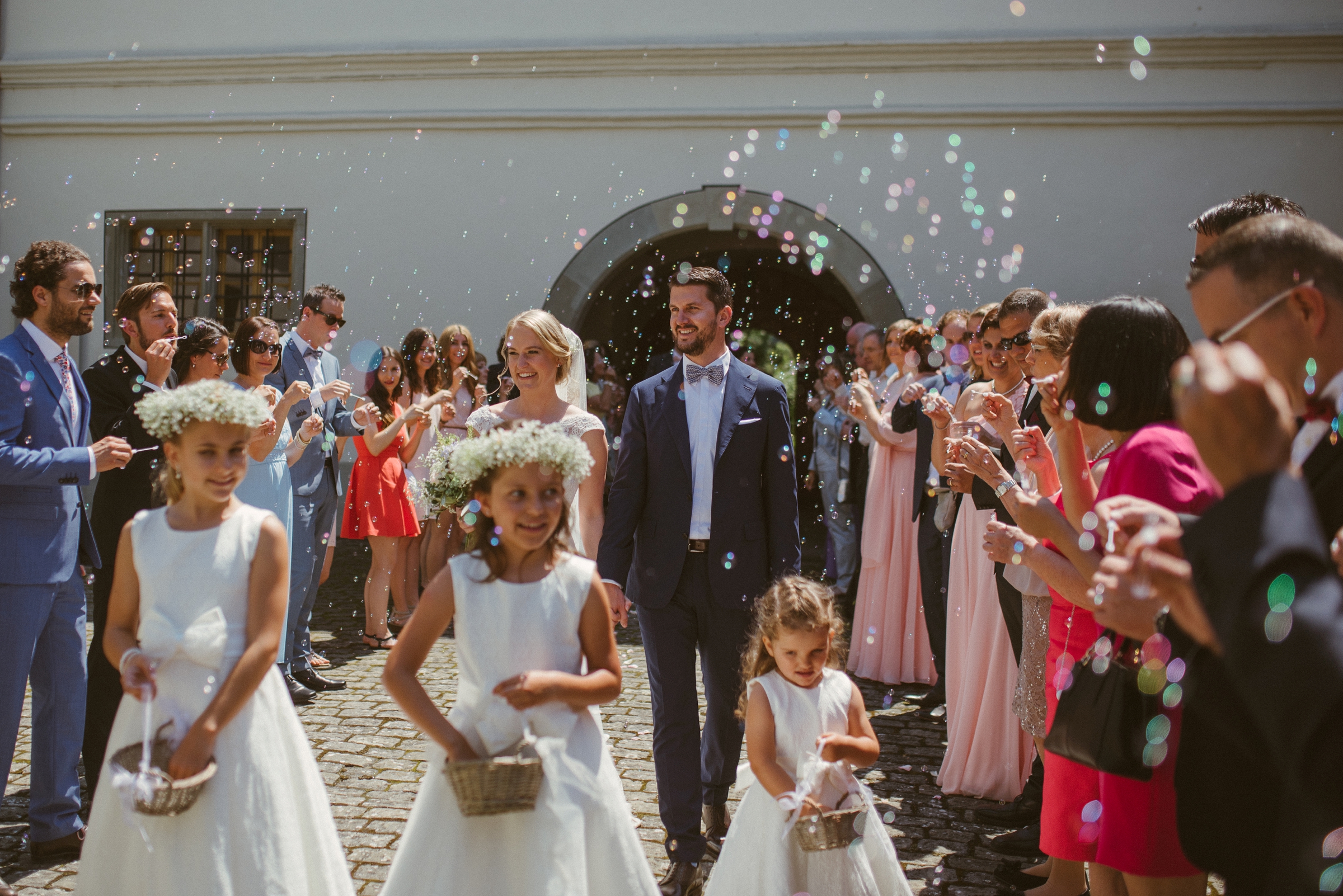 Hochzeit in der Schweiz: Brautpaar kommt nach der Trauung aus der Kirche, Blumenmädchen streuen Blumen, es fliegen Seifenblasen