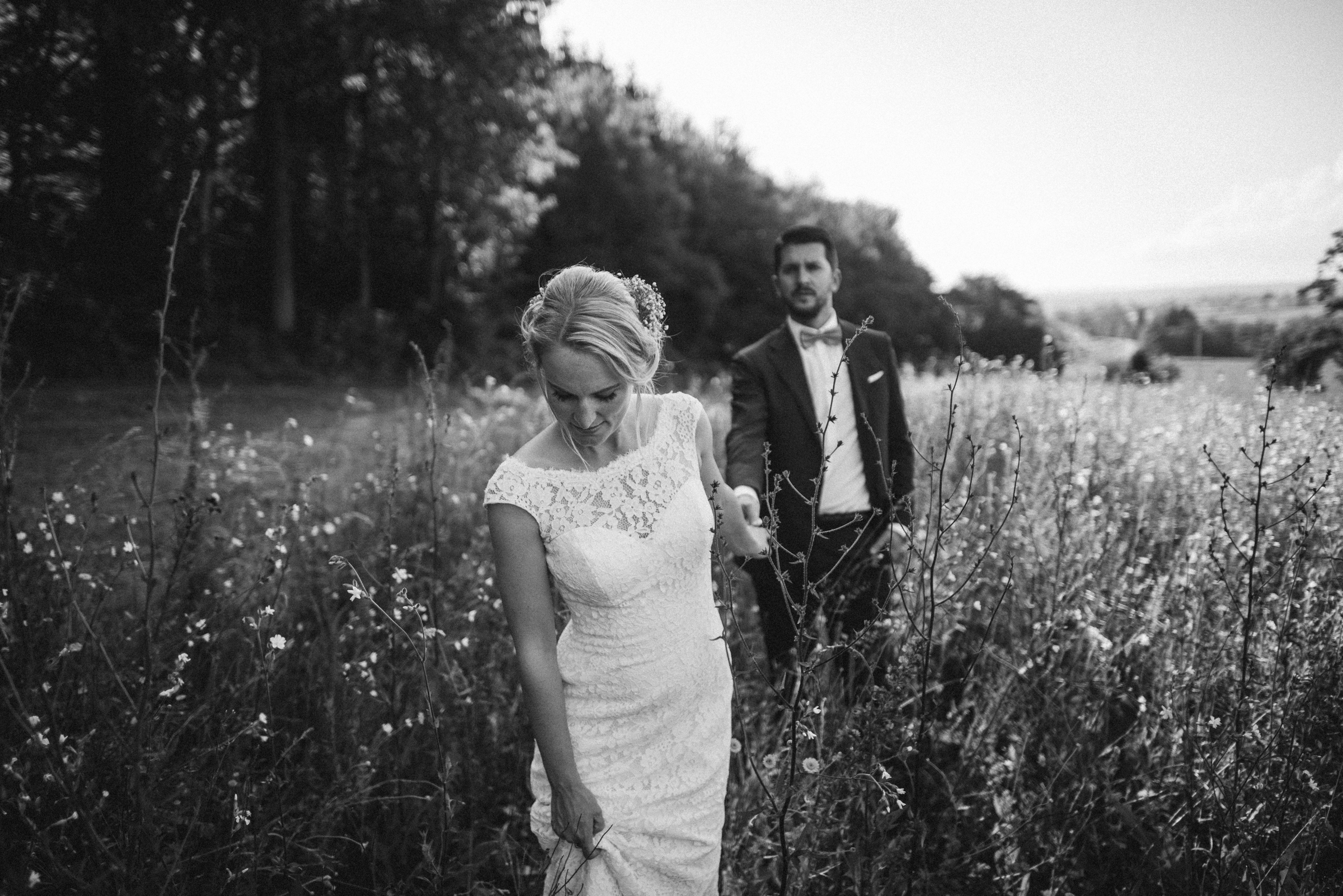 Hochzeit in der Schweiz: Brautpaar läuft Hand in Hand durch eine Sommerwiese
