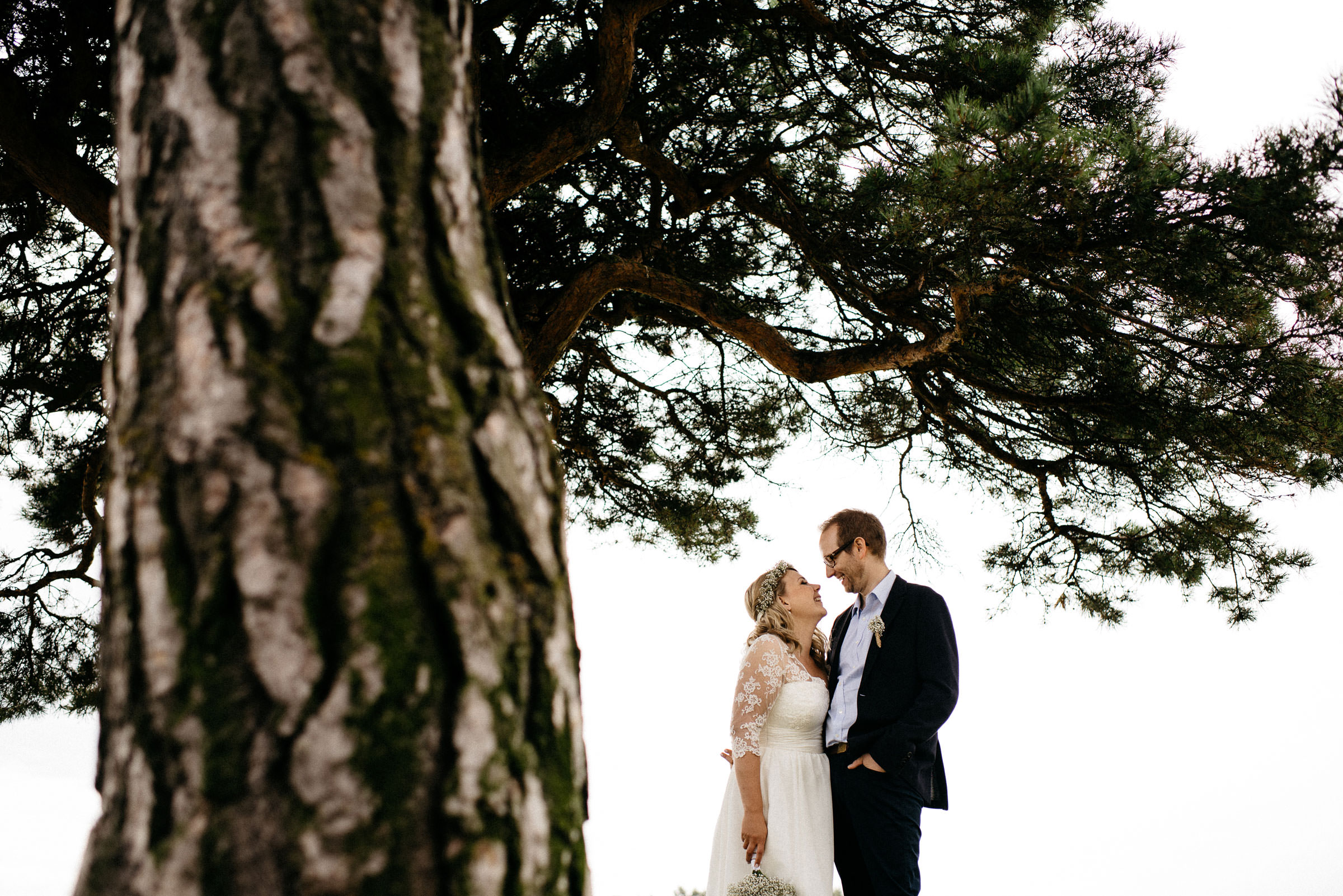 finnische Hochzeit: das Brautpaar steht neben einem Baum und lacht sich an
