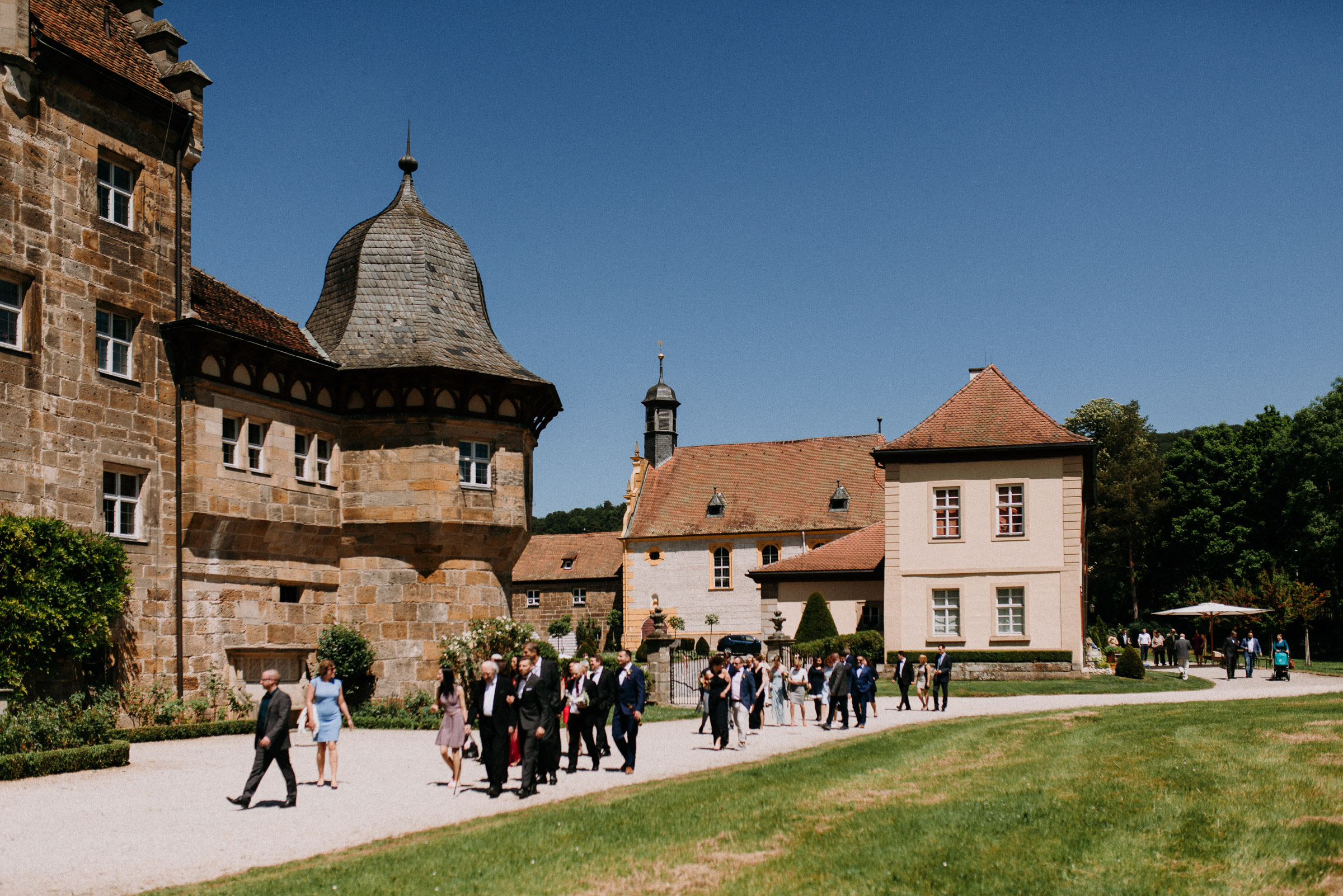 Deutsch-türkische Hochzeit: Hochzeitsgesellschaft läuft vor dem Schloss Eyrichshof entlang, der Himmel ist strahlend blau
