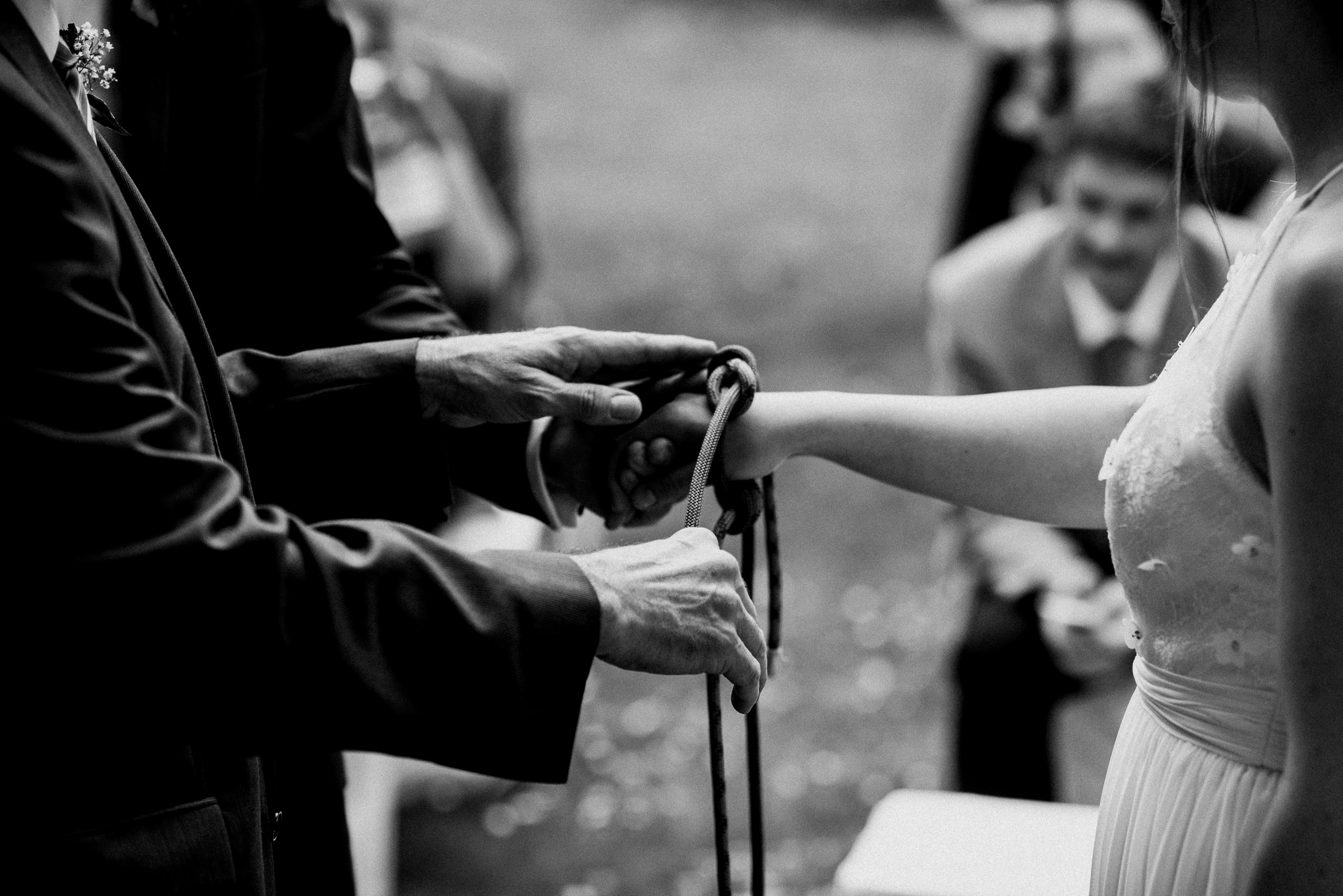 Outdoor-Hochzeit: Handfasting-Zeremonie, Bräutigam legt das Kletterseil um das Handgelenk der Braut