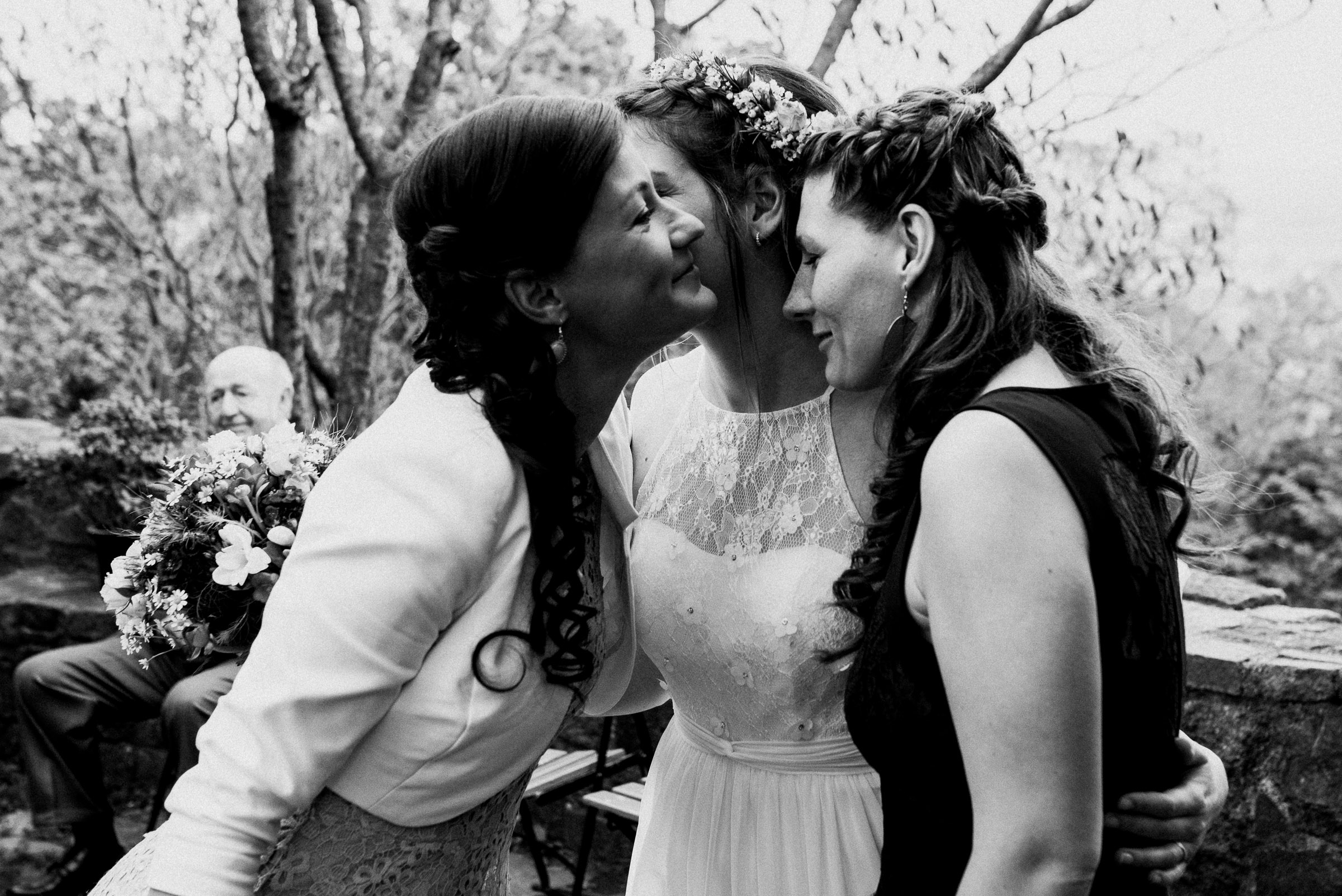 Outdoor-Hochzeit: zwei Hochzeitsgäste umarmen die Braut rechts und links