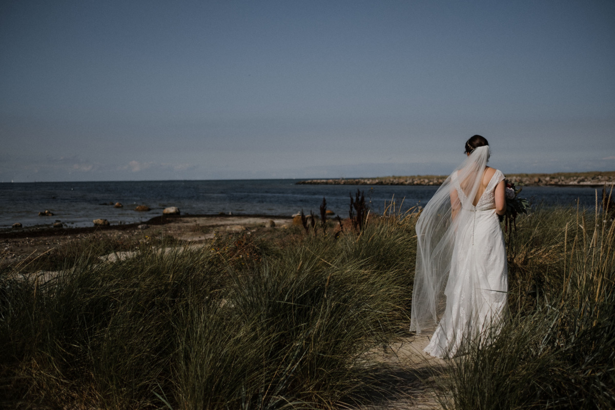 Strandhochzeit in Kiel: Rückenaufnahme der Braut, die aufs Meer blickt.