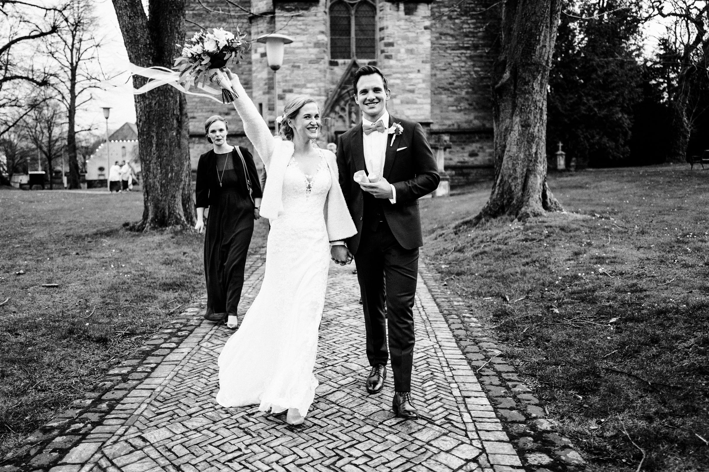 Auszug des Brautpaars der Silvester-Hochzeit aus der Kirche, die Braut hebt den Brautstrauß in die Höhe
