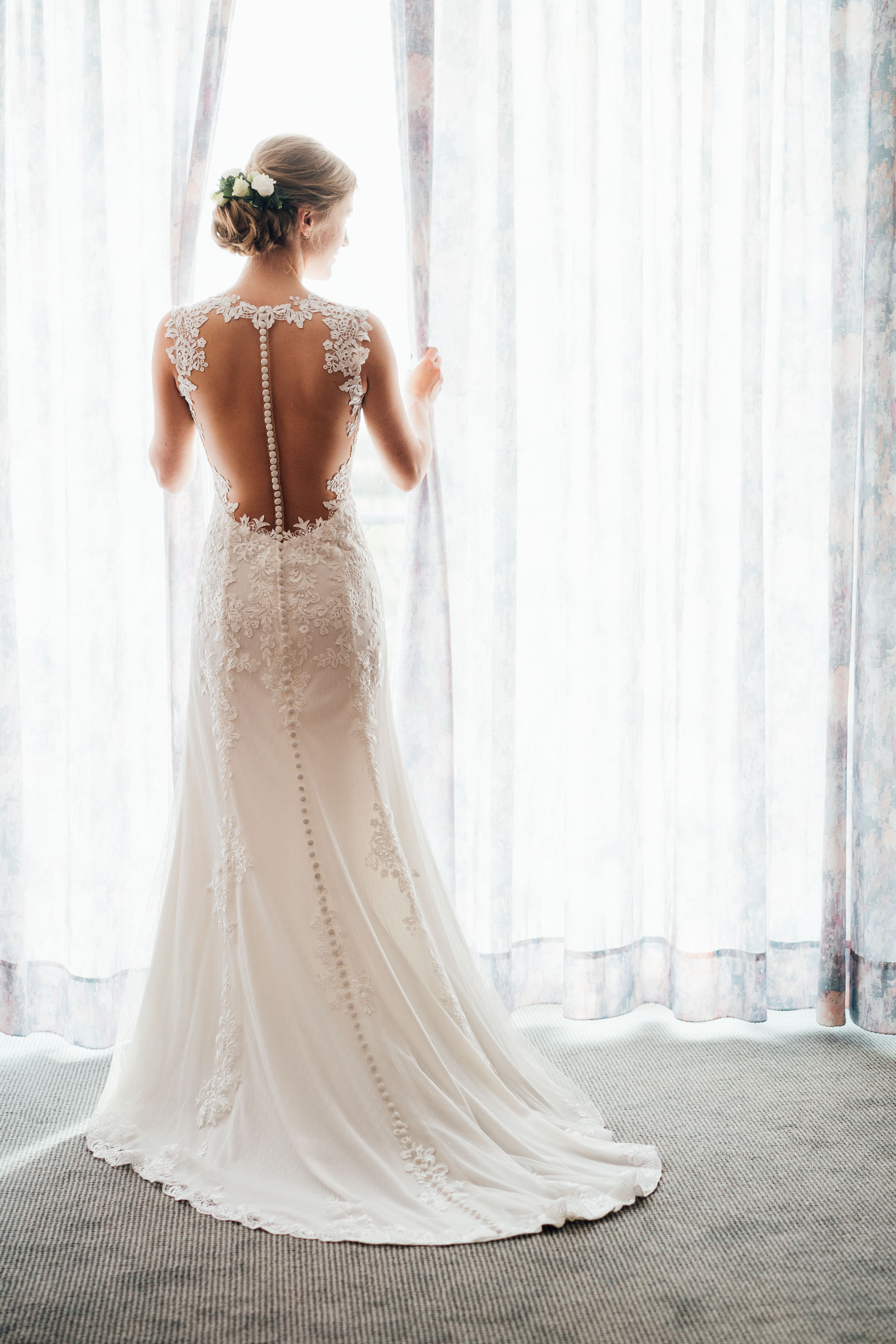 die Braut der Silvester-Hochzeit vor dem Fenster in einem bodenlangen, weißen Brautkleid