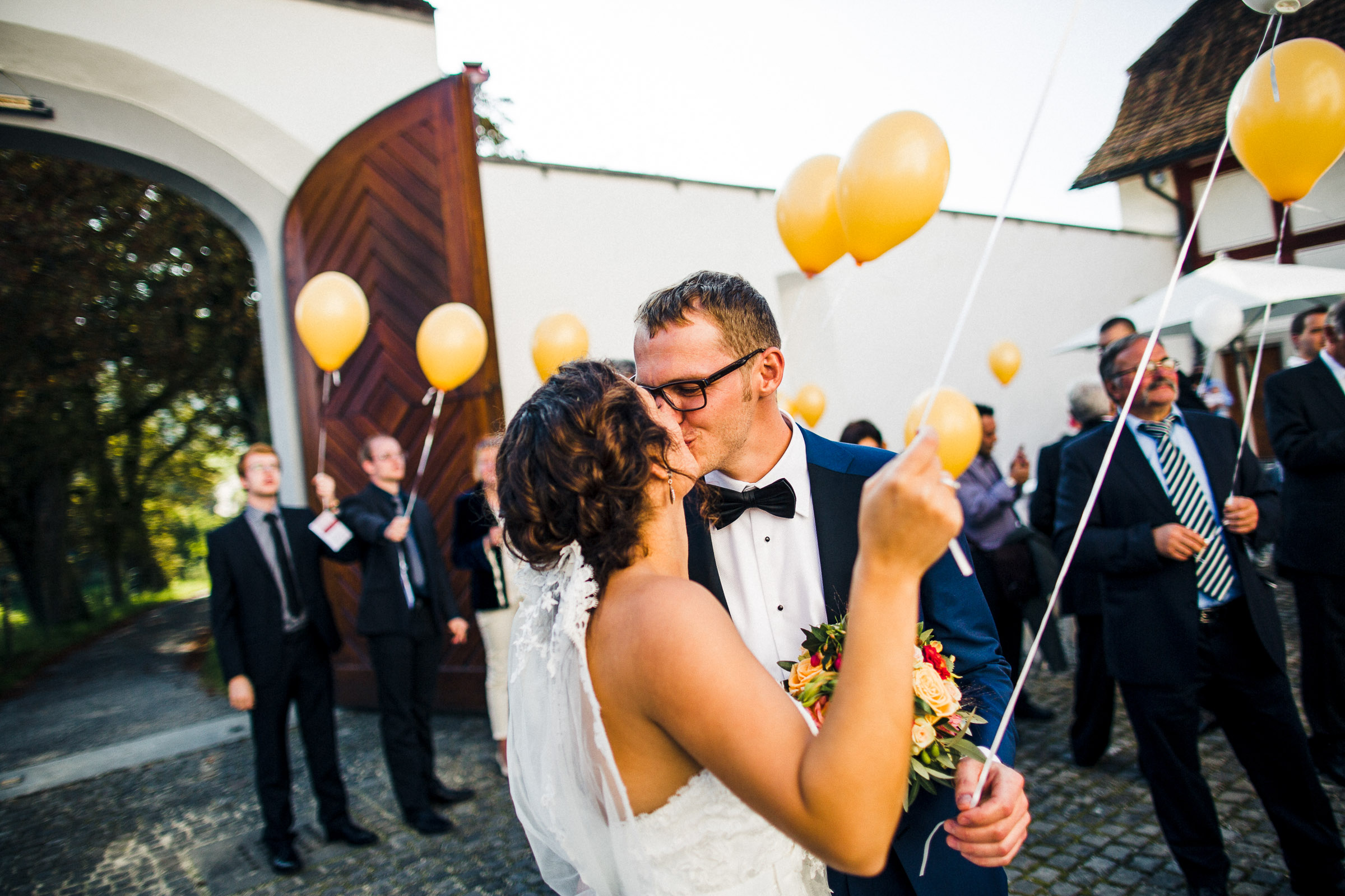 Schlosshochzeit: alle halten Ballons in den Händen, Brautpaar küsst sich