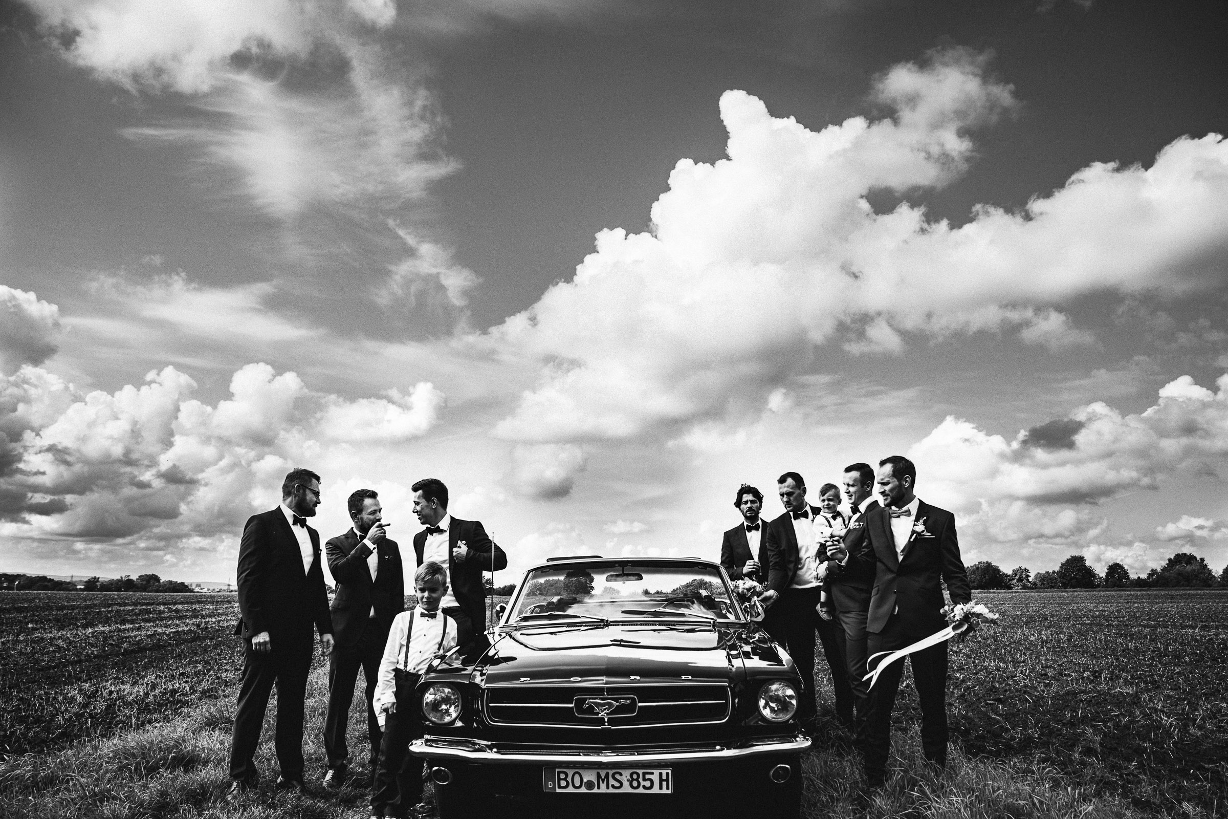 Septemberhochzeit: männliche Hochzeitsgäste mit Bräutigam und Mustang auf einer Wiese