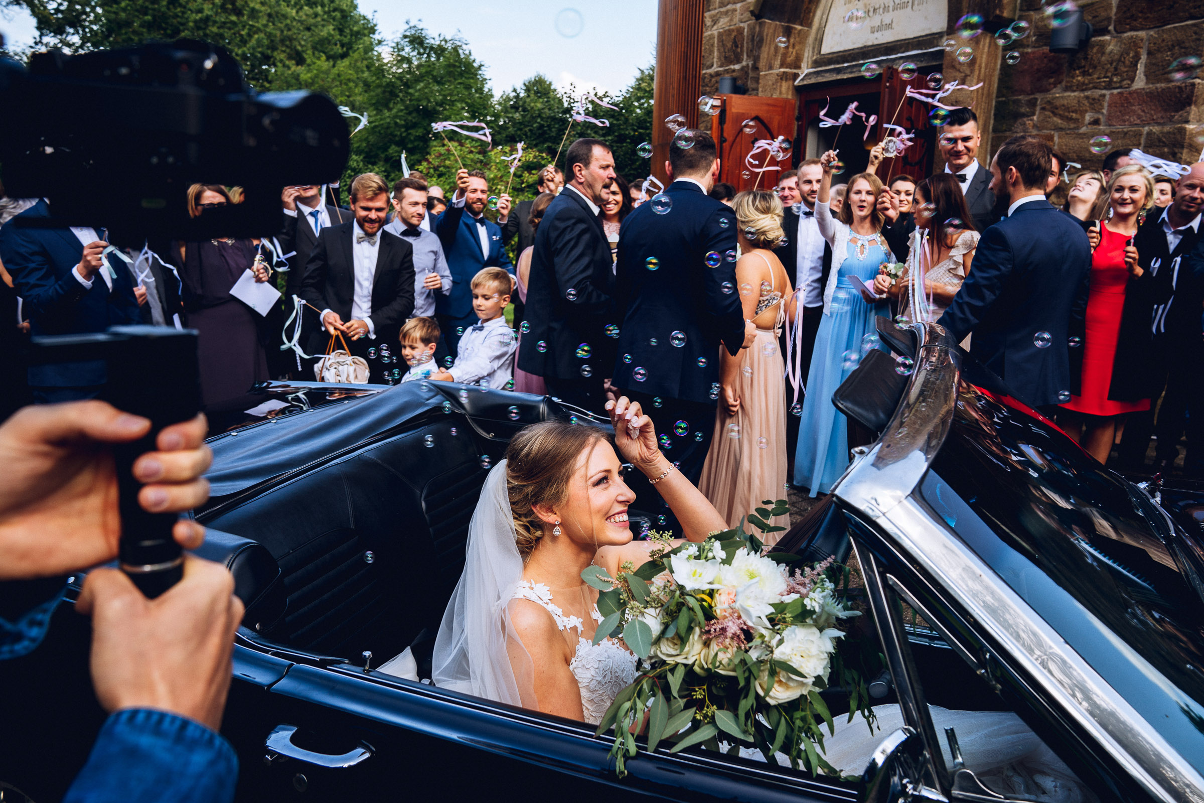Septemberhochzeit: Braut sitzt im Hochzeitsauto, es fliegen Seifenblasen