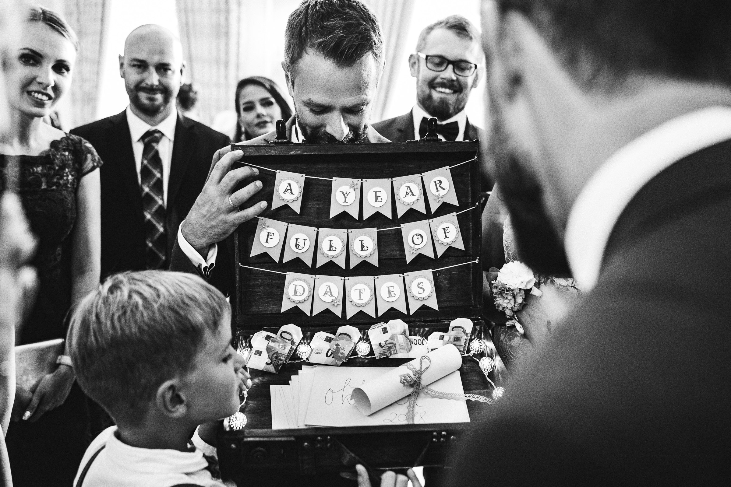 Septemberhochzeit: Bräutigam öffnet gerührt ein Hochzeitsgeschenk, eine Truhe mit Gutscheinen für Treffen mit den Hochzeitsgästen im folgenden Jahr
