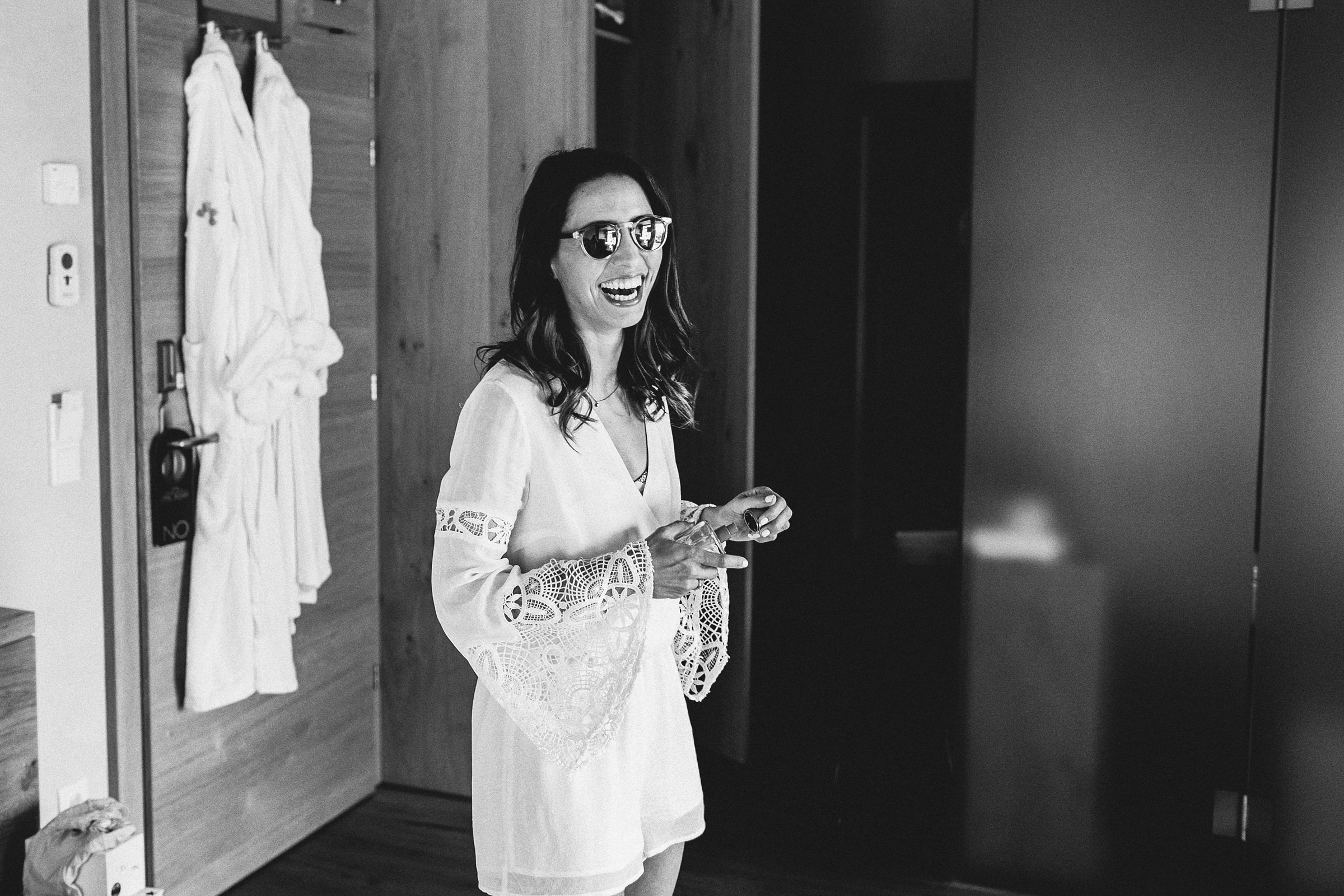 die Braut der mediterranen Hochzeit lachend mit Sonnenbrille im Hotelzimmer