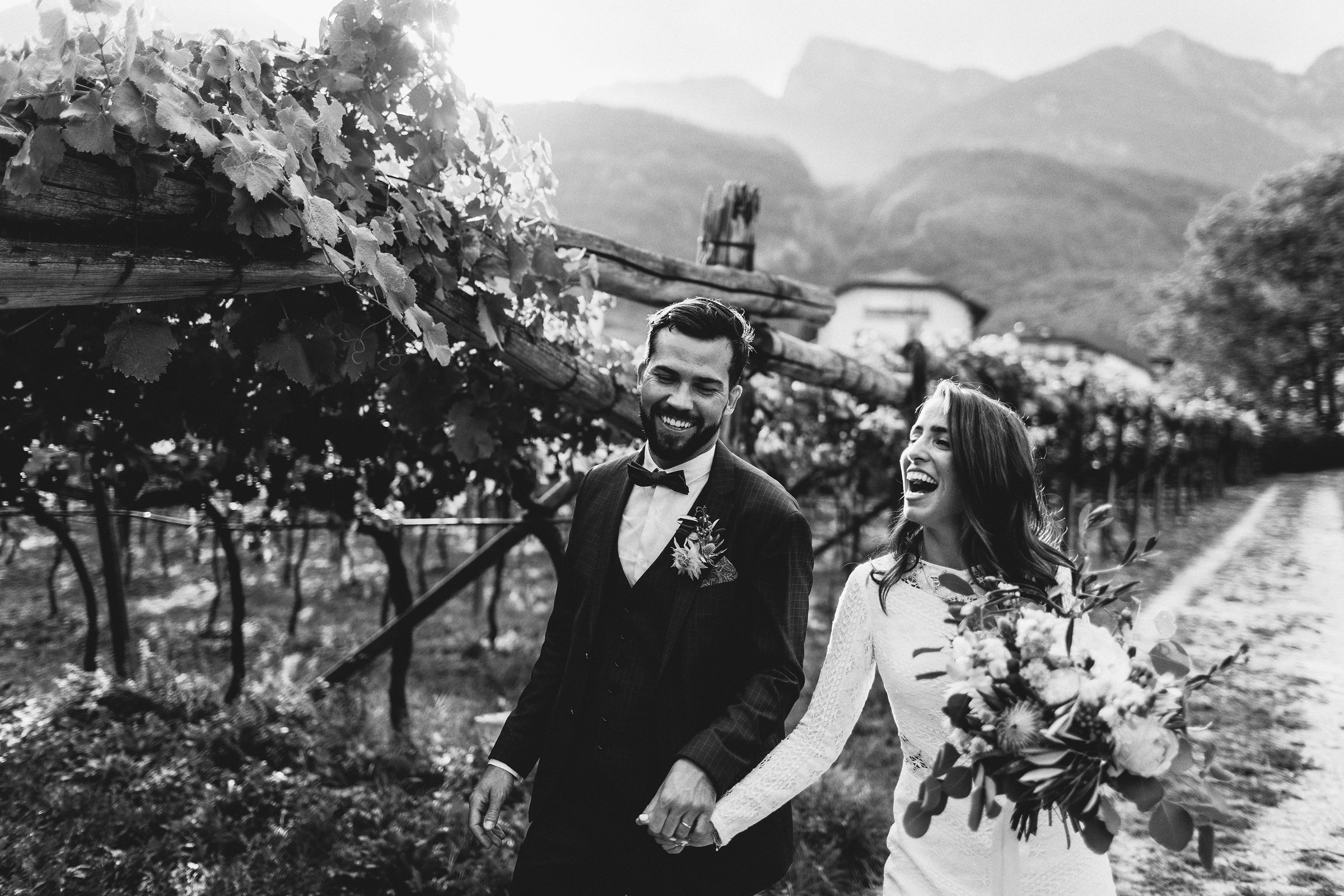 Brautpaar der mediterranen Hochzeit läuft Hand in Hand lachend durch die Weinreben
