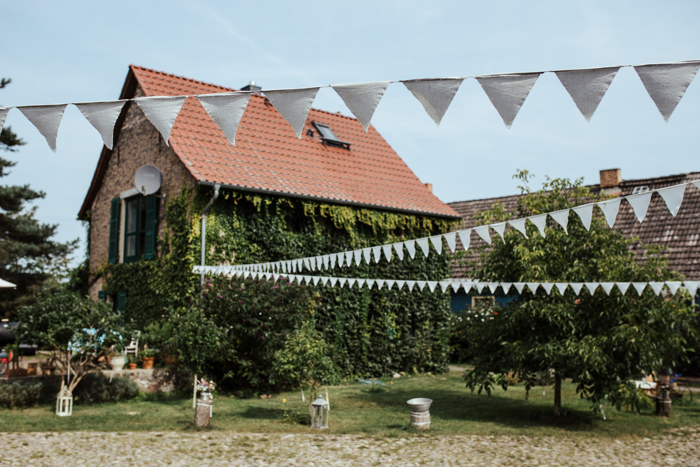 weiße Wimpel flattern über dem Garten der Location für die Scheunenhochzeit