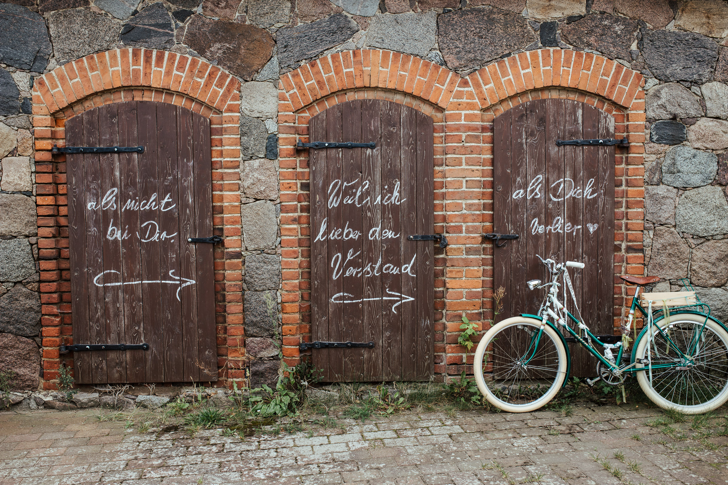 Drei kleine Tore der Scheune, mit Kreide aufgemalte Sprüche zur Scheunenhochzeit, rechts ein Fahrrad