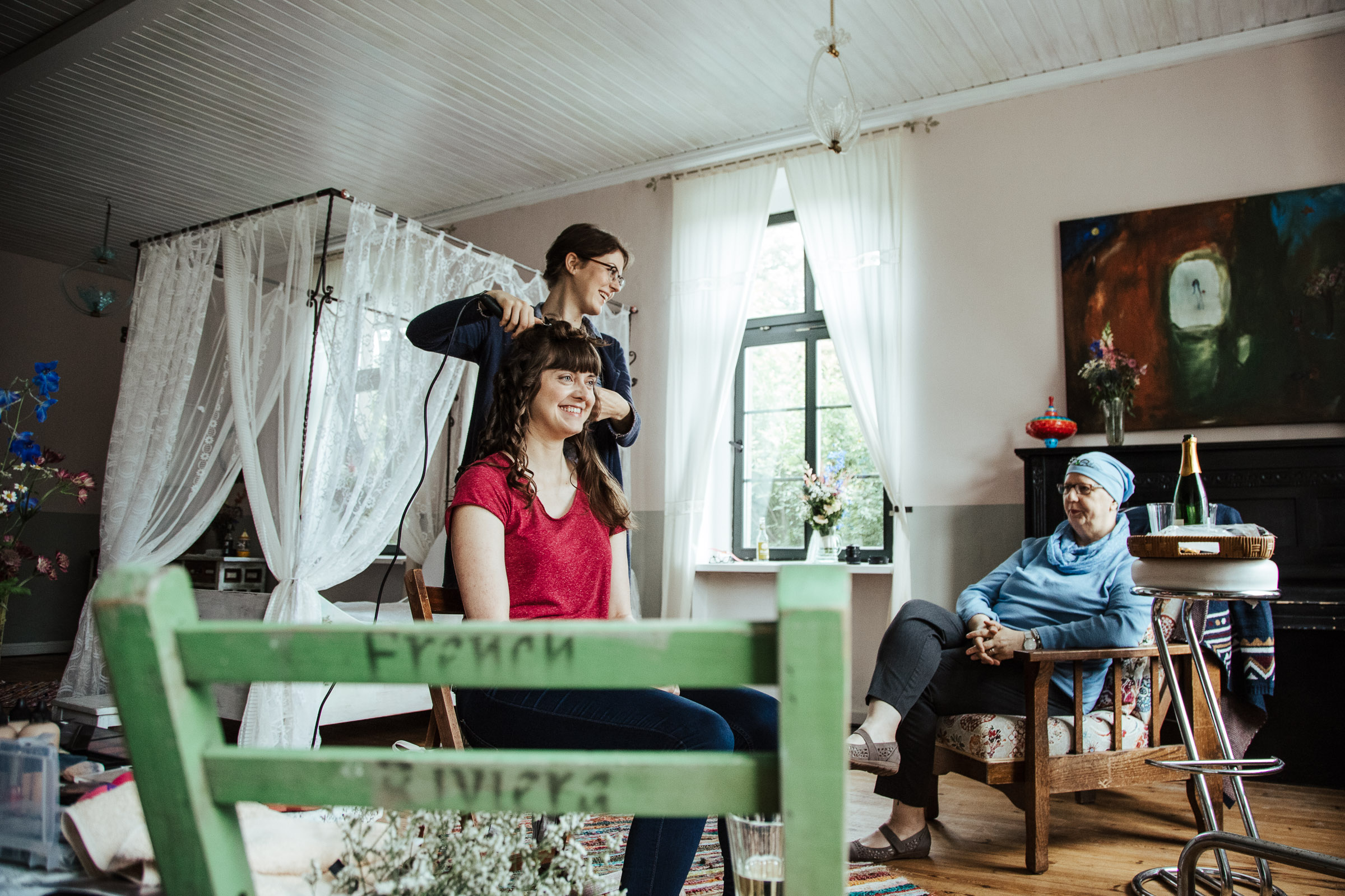 Braut mit Familie im Brautzimmer, Schwester onduliert der Braut die Haare für die Scheunenhochzeit