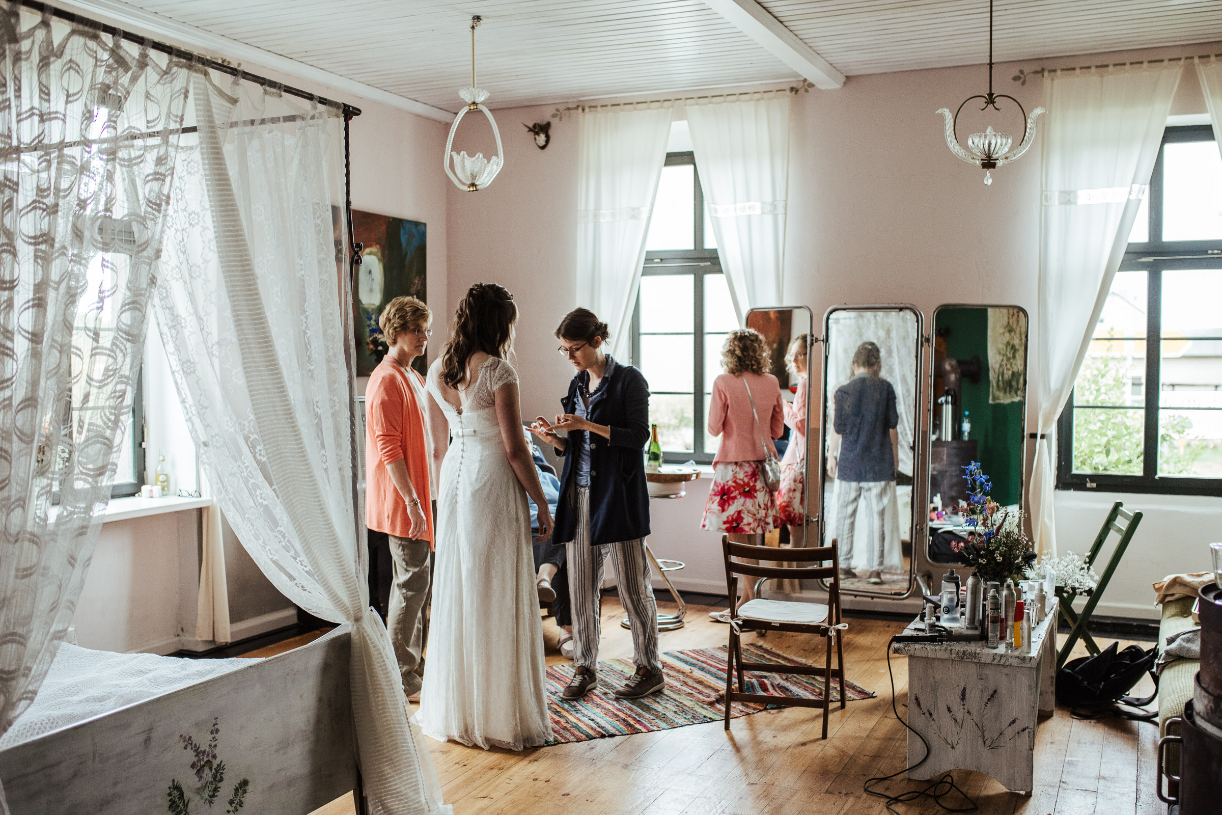 weibliche Gäste im Zimmer der Braut helfen der Braut beim Anziehen für die Scheunenhochzeit