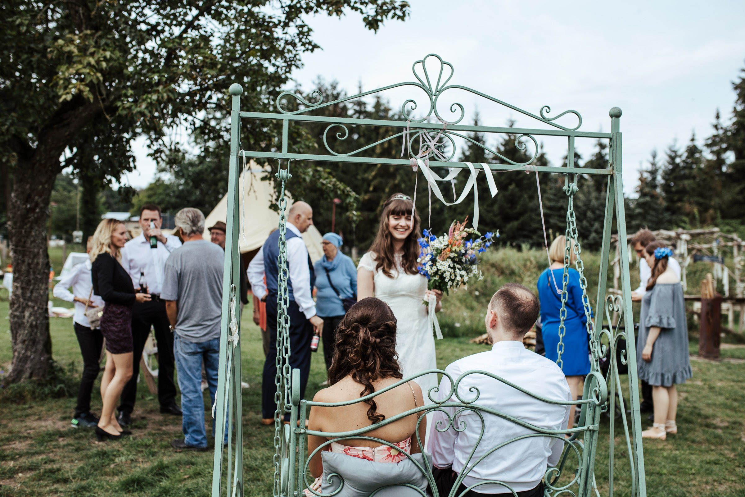 im Garten der Scheunenhochzeit, zwei Gäste sitzen in einer Hollywoodschaukel, Braut lacht