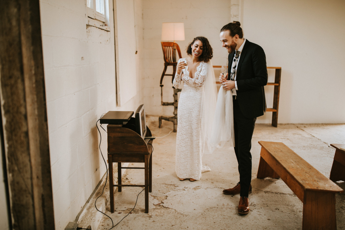 Hochzeit in New York - Brautpaar steht lachend vor einem Minifernseher und schaut ein Video