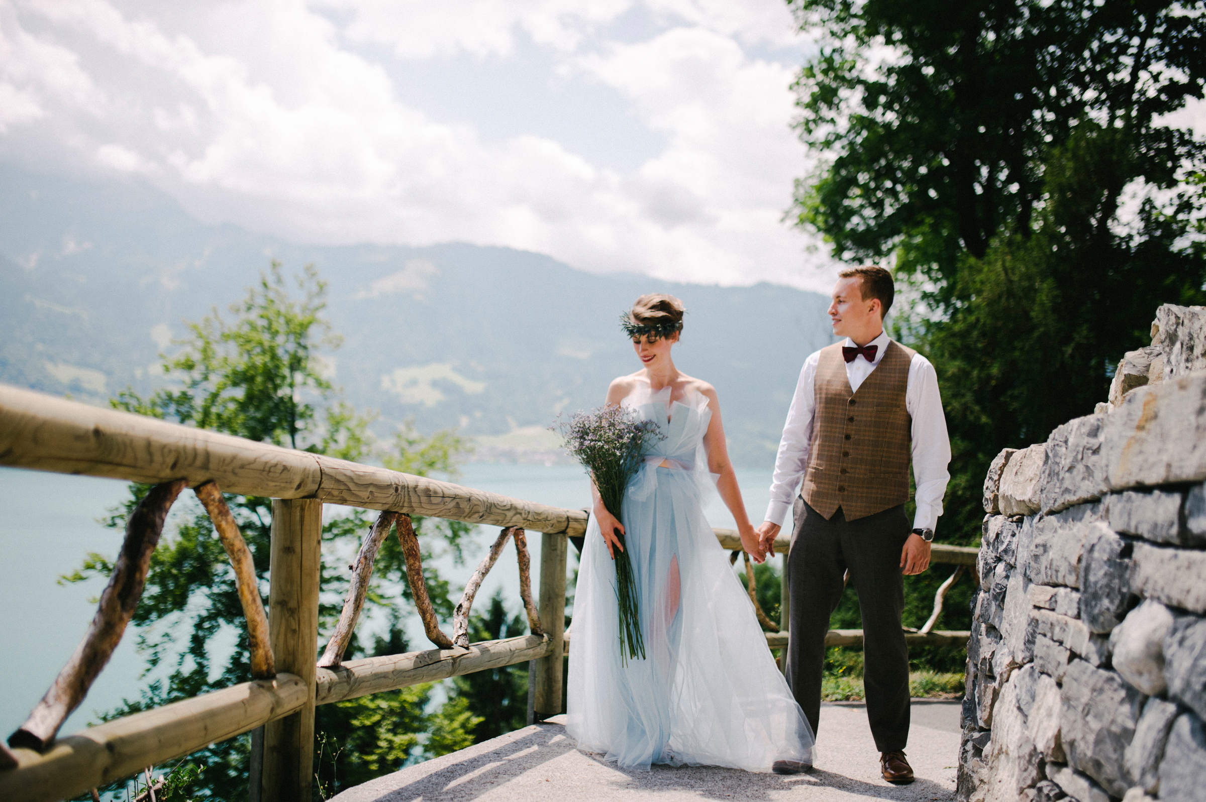 Berghochzeit: Brautpaar Hand in Hand im Sonnenschein vor Bergsee-Panorama