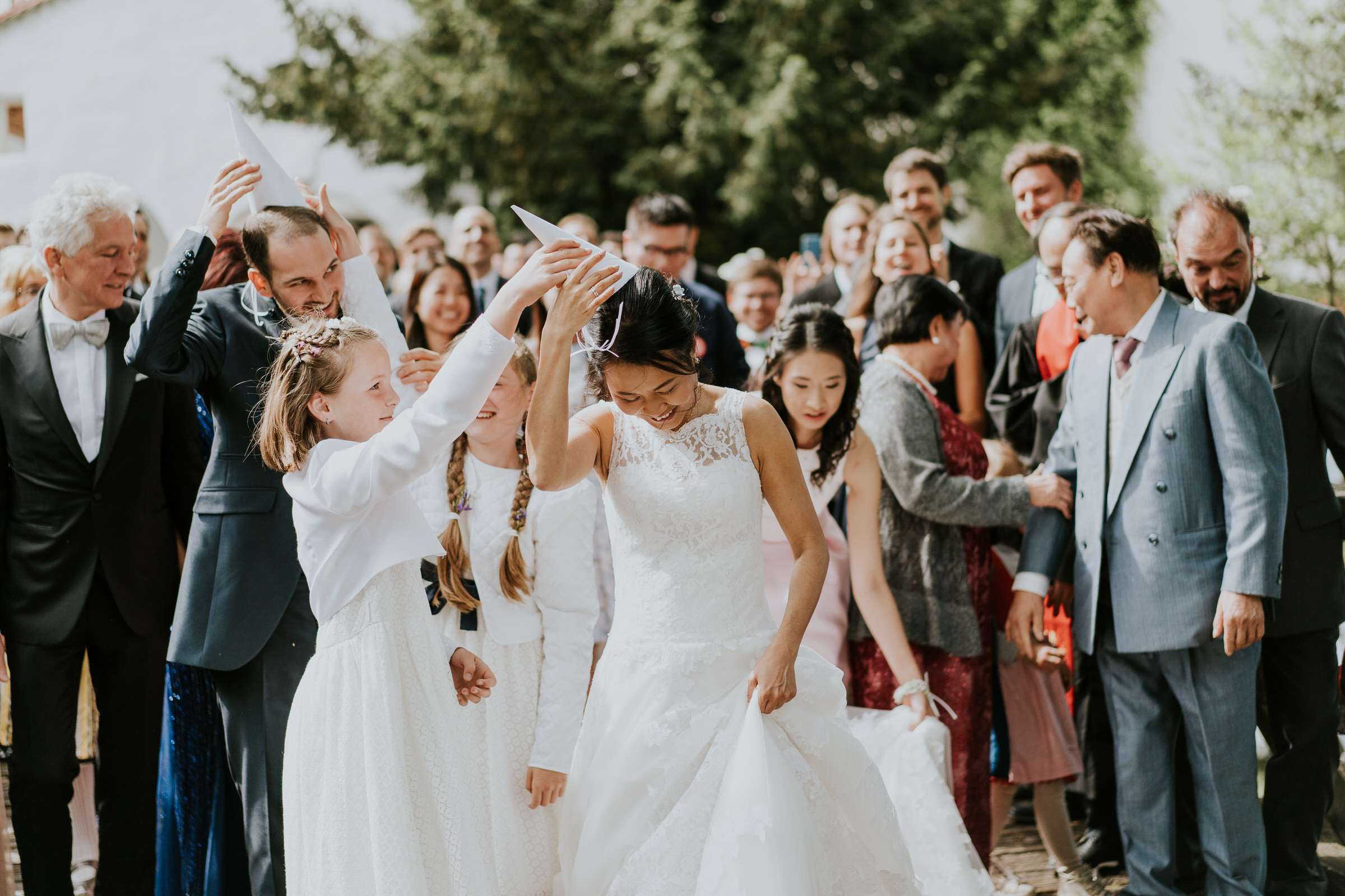 Deutsch-chinesische Hochzeit: Braut bekommt einen weißen Papierhut aufgesetzt von einem Blumenmädchen