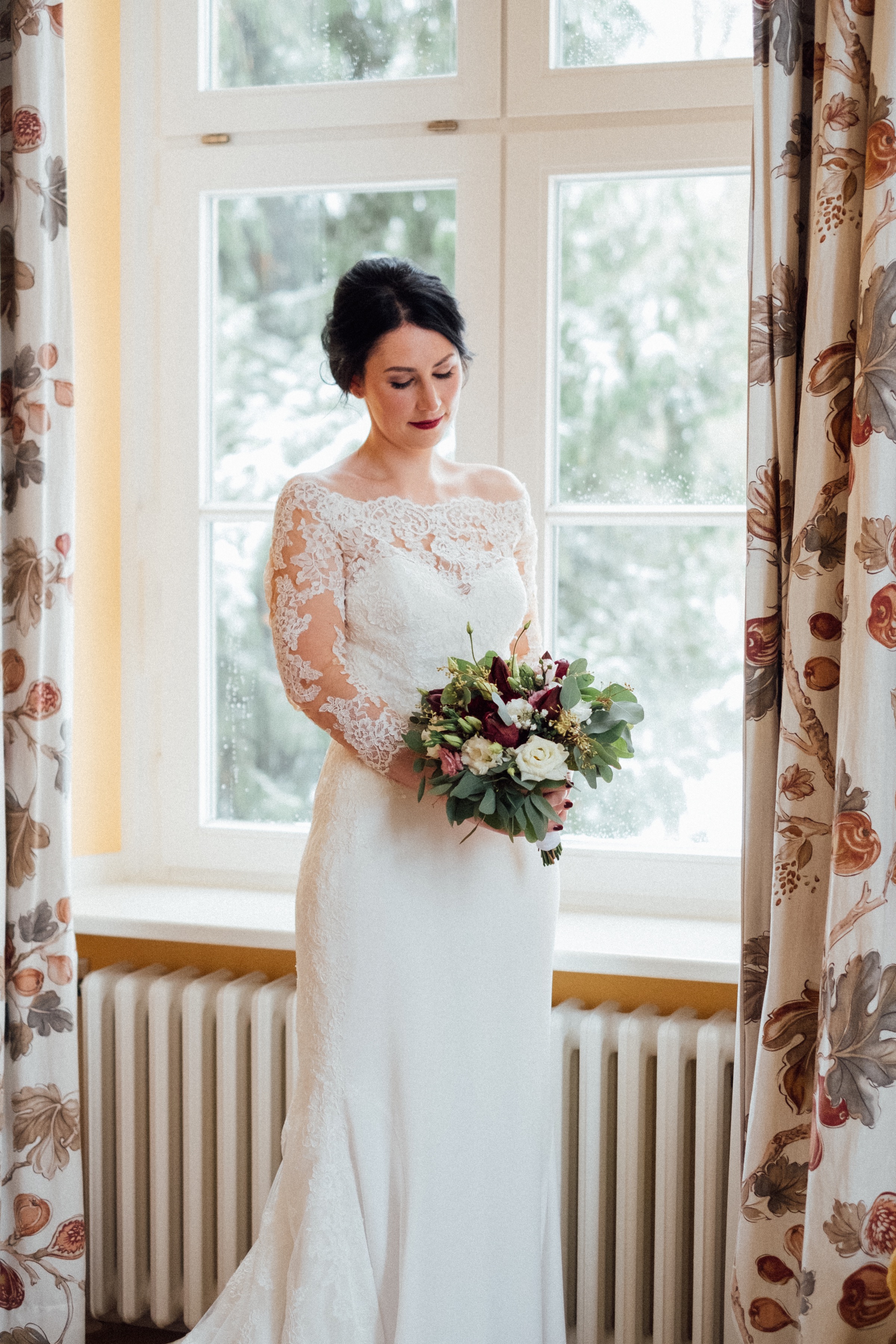 Winterhochzeit: Braut mit Brautstrauß am Fenster
