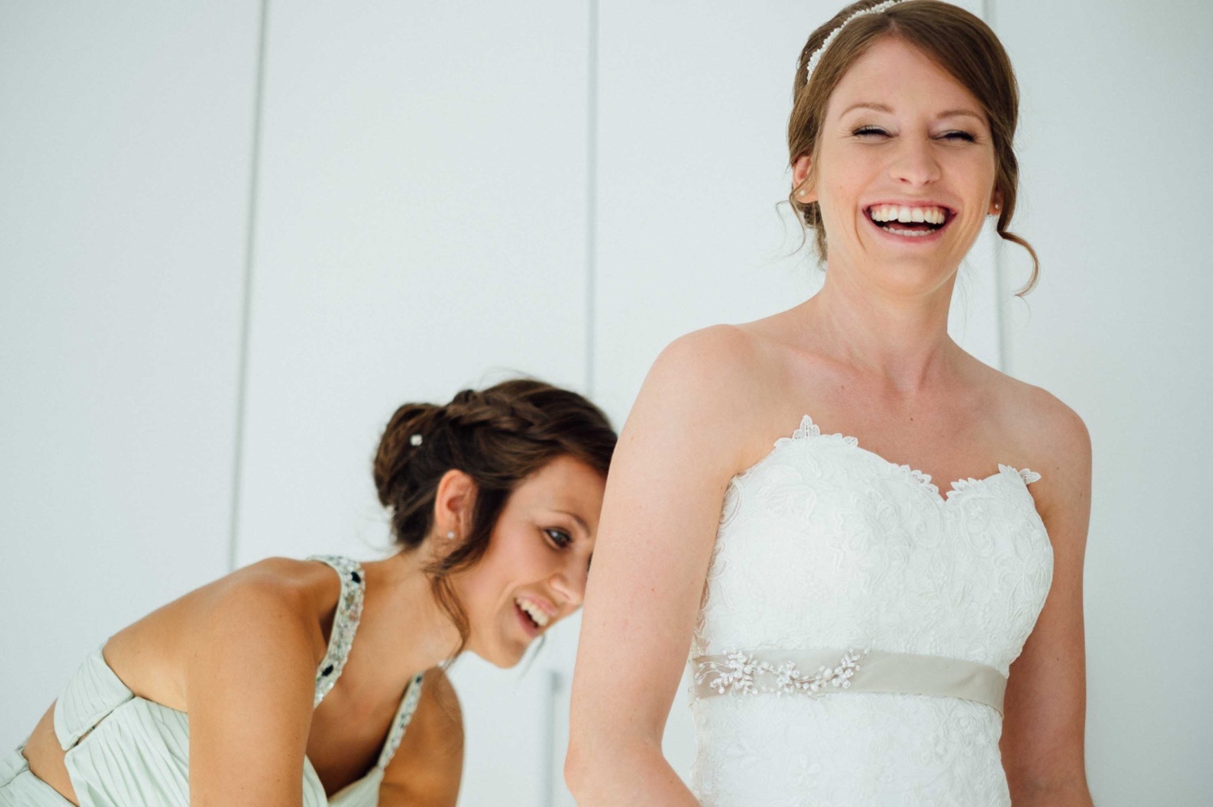 Hochzeit in Bremen: Trauzeugin hilft beim Verschließen des Brautkleids, Braut lacht strahlend