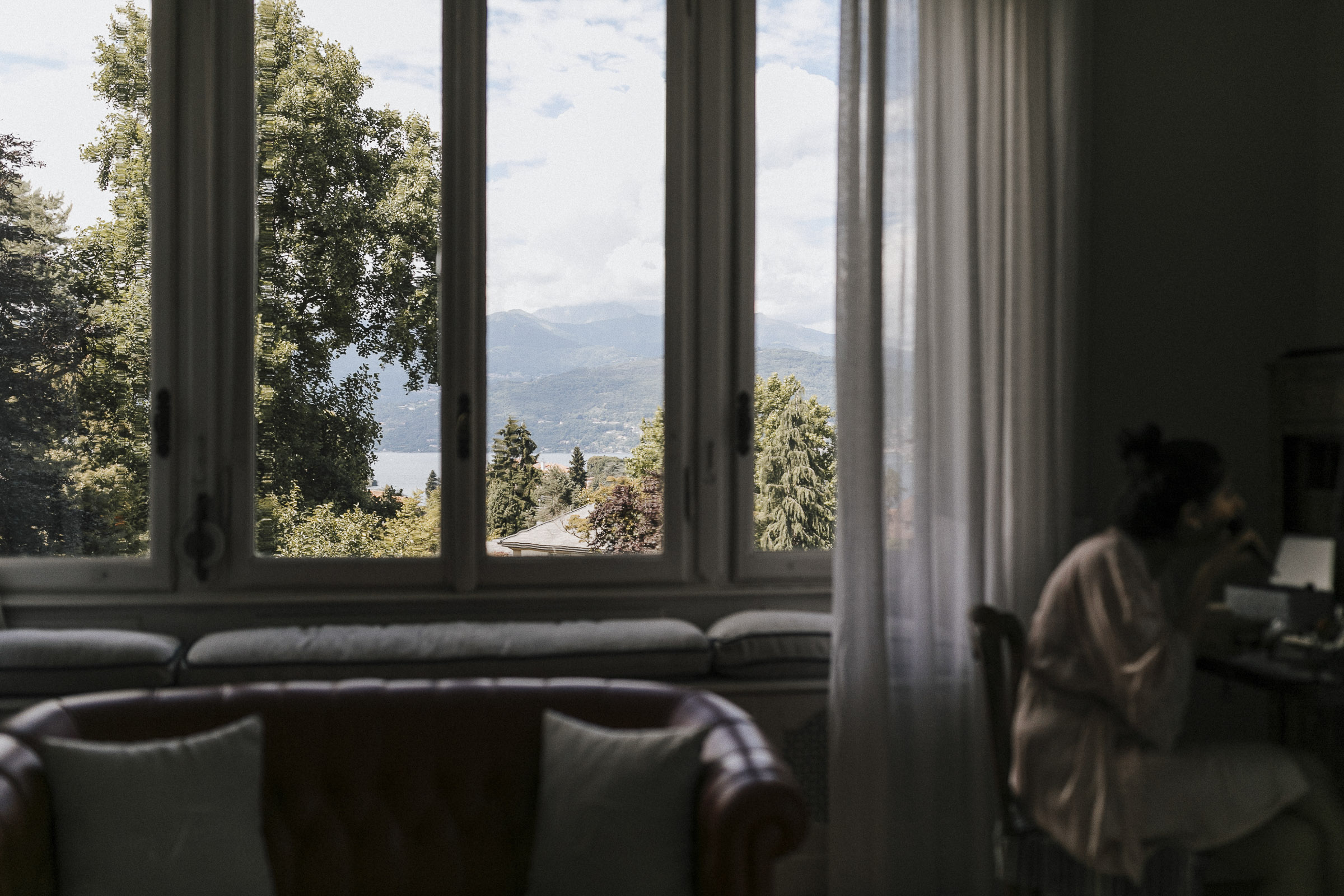 Hochzeit in Italien: Blick durch das Fenster des Brautzimmers auf den Lago Maggiore, im Vordergrund schminkt sich die Braut