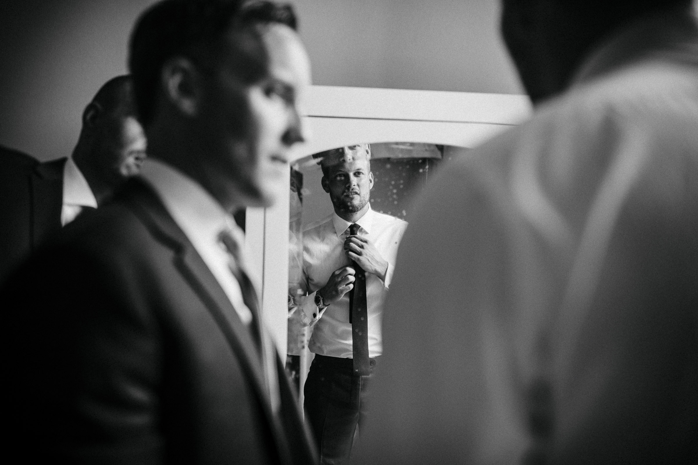 Hochzeit in Italien: Bräutigam schaut in den Spiegel und richtet sich die Krawatte, Trauzeugen stehen um ihn herum