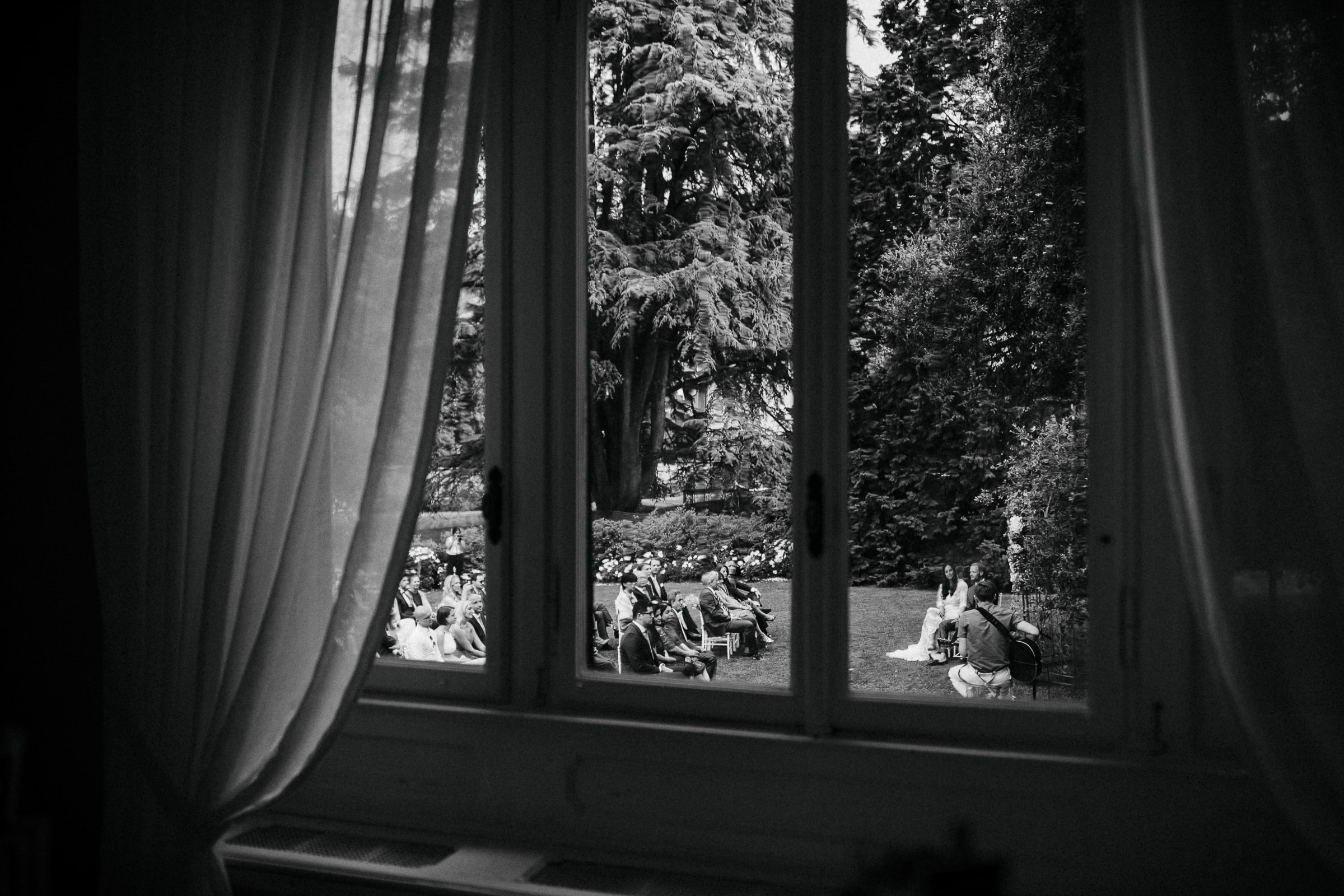 Hochzeit in Italien: Blick durch ein Fenster der Villa in den Garten in dem gerade die Trauung stattfindet.