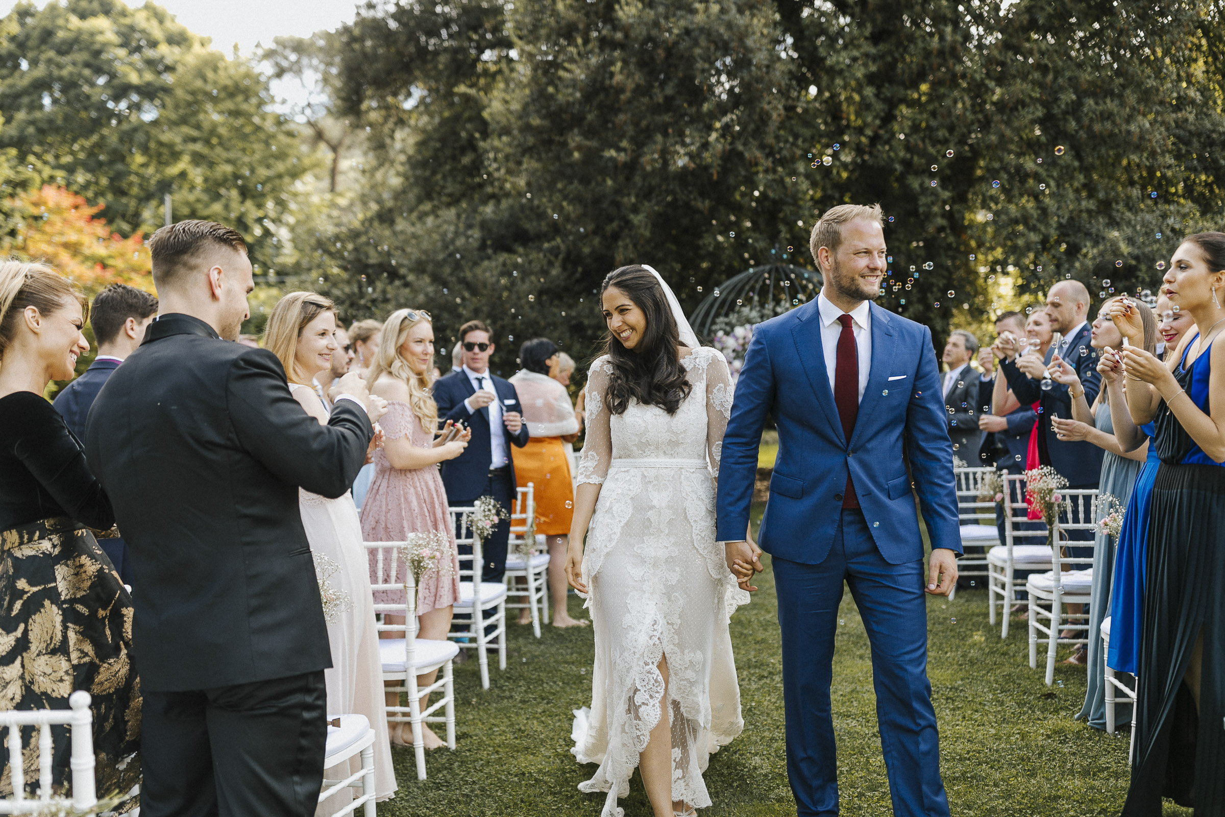 Hochzeit in Italien: das Brautpaar läuft Hand in Hand durch die jubelnde Hochzeitsgesellschaft