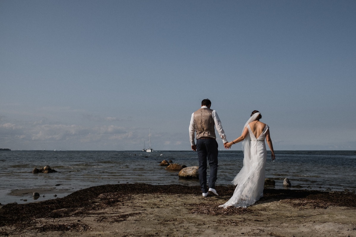 Strandhochzeit in Kiel: Brautpaar geht Hand in Hand in Richtung Meer.