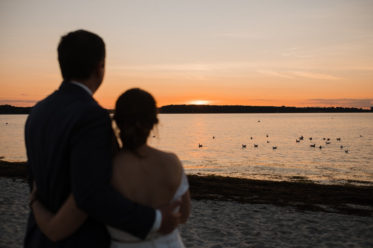 Strandhochzeit in Kiel: Brautpaar schaut auf den Sonnenuntergang.