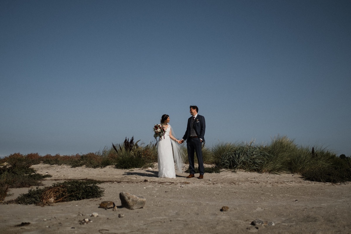 Strandhochzeit in Kiel: Brautpaar steht in den Dünen und schaut sich an.
