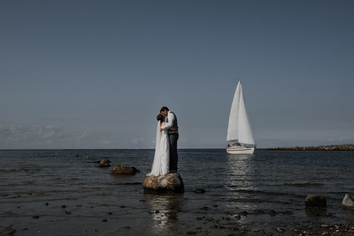Strandhochzeit in Kiel: Das Brautpaar steht mitten im Meer auf Steinen.