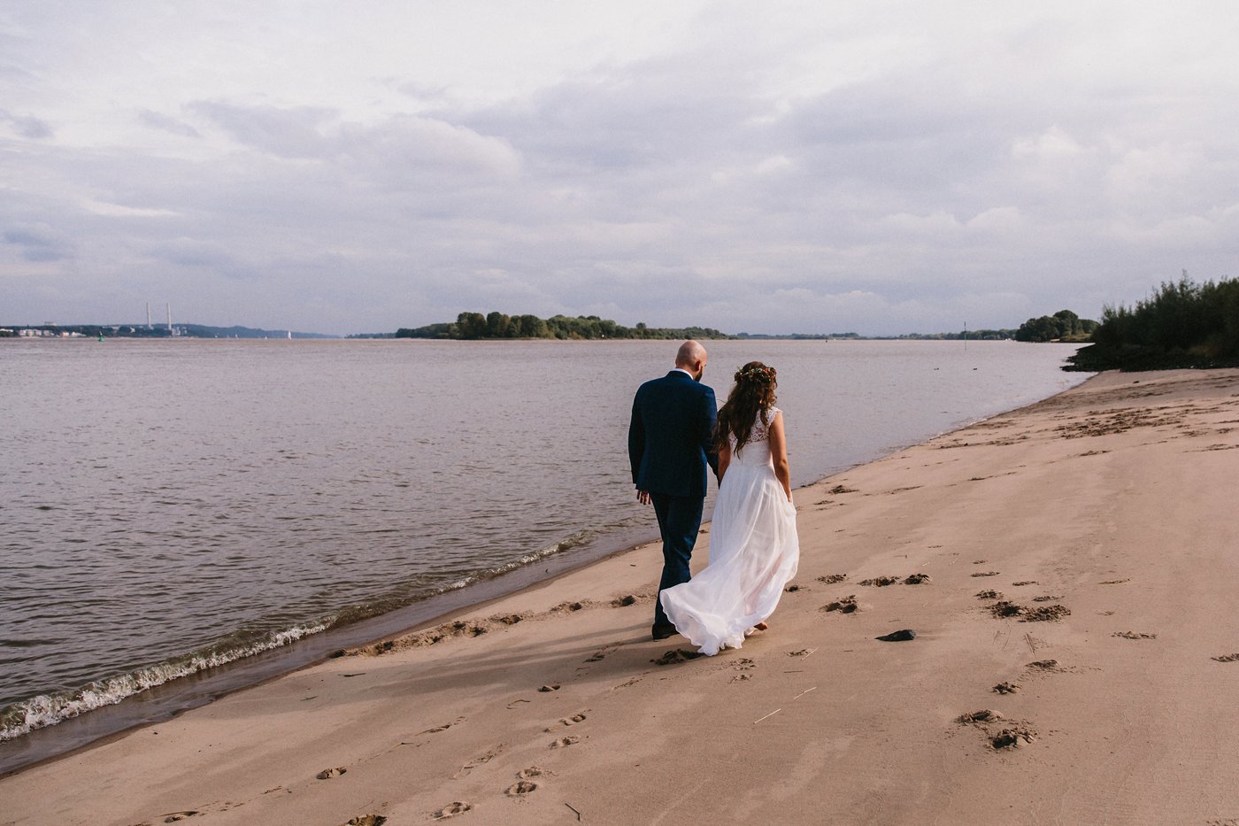 Urbane Hochzeit: Brautpaar läuft Hand in Hand am Elbstrand entlang