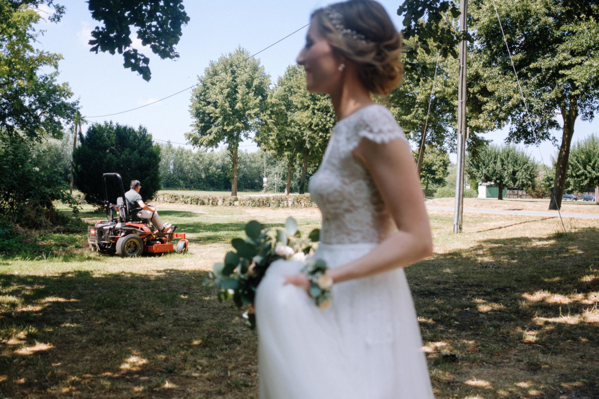 Vintage-Hochzeit: die Braut läuft an einem Mann vorbei, der den Rasen mäht