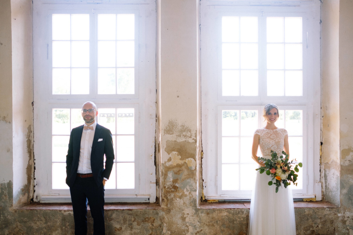 Vintage-Hochzeit: Brautpaar steht nebeneinander vor zwei Fenstern