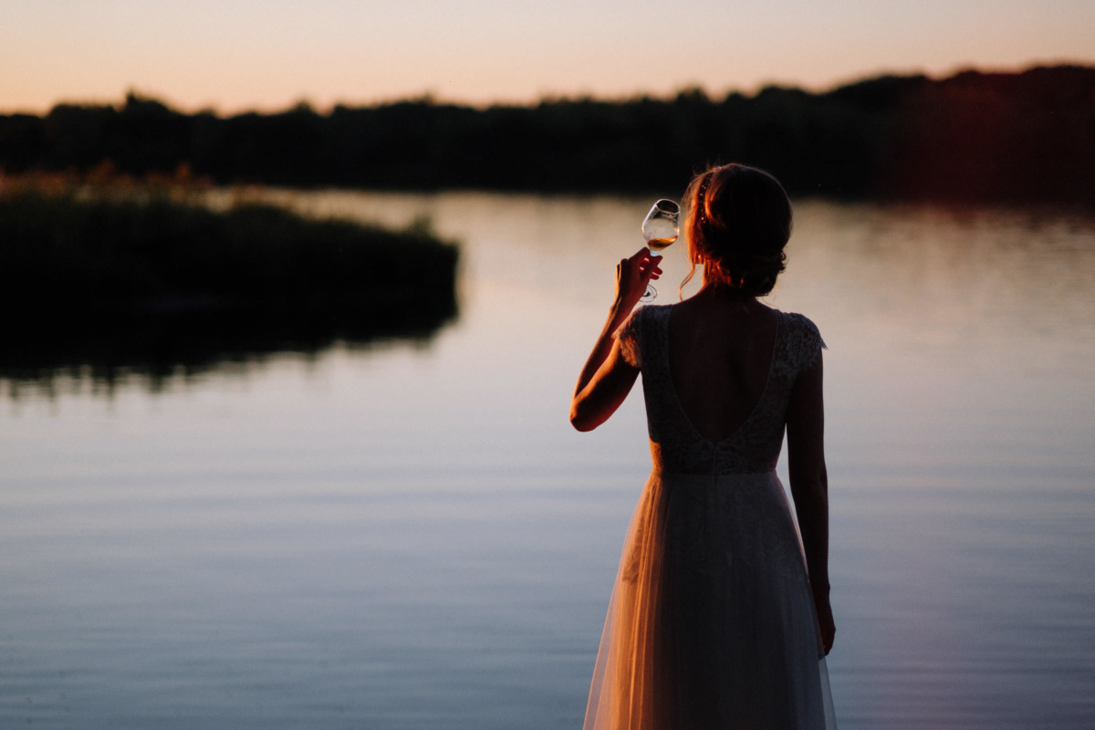 Vintage-Hochzeit: Braut trinkt Wein und schaut in den Sonnenuntergang