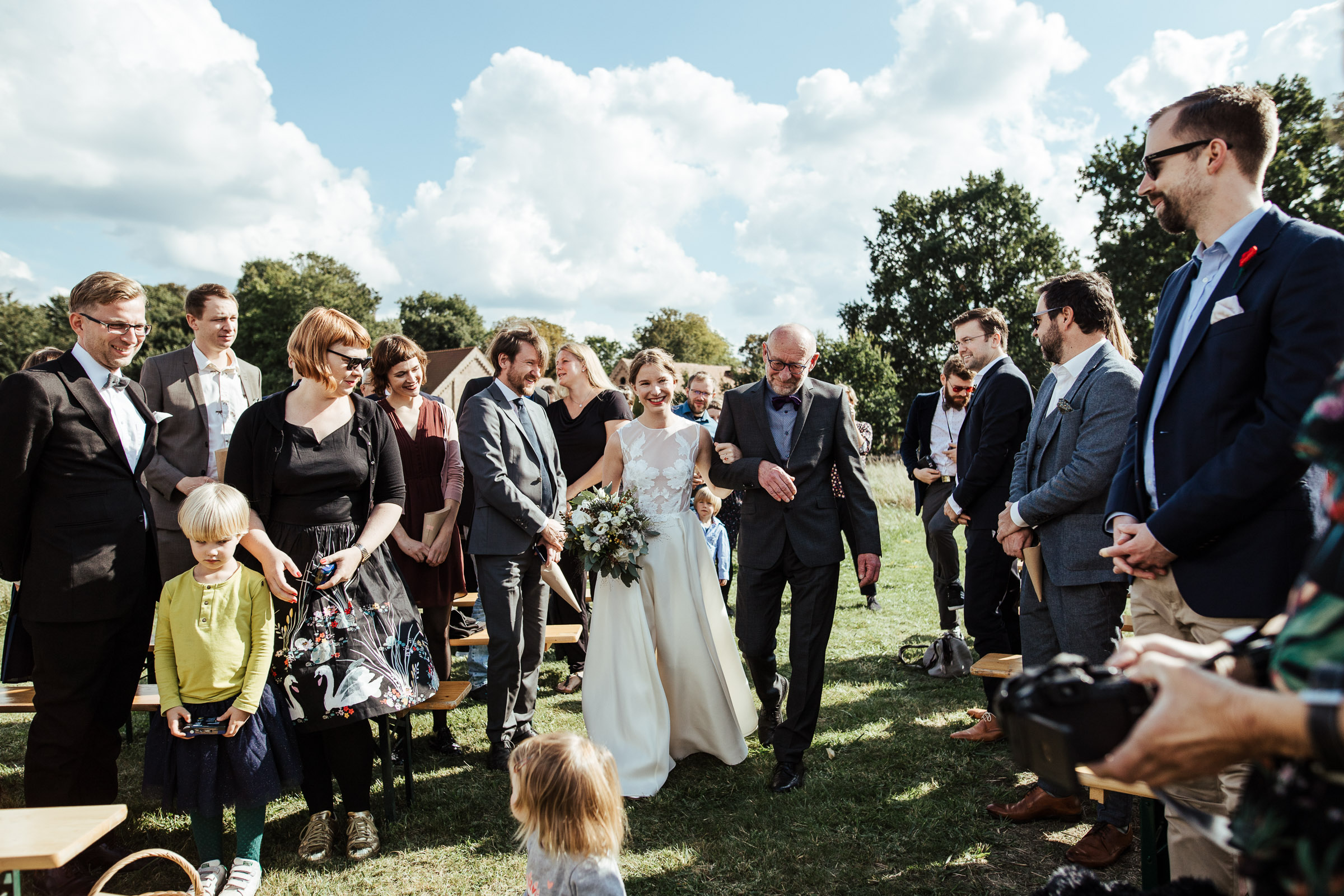 Landhochzeit: Braut wird vom Brautvater durch das Spalier der Hochzeitsgäste geführt