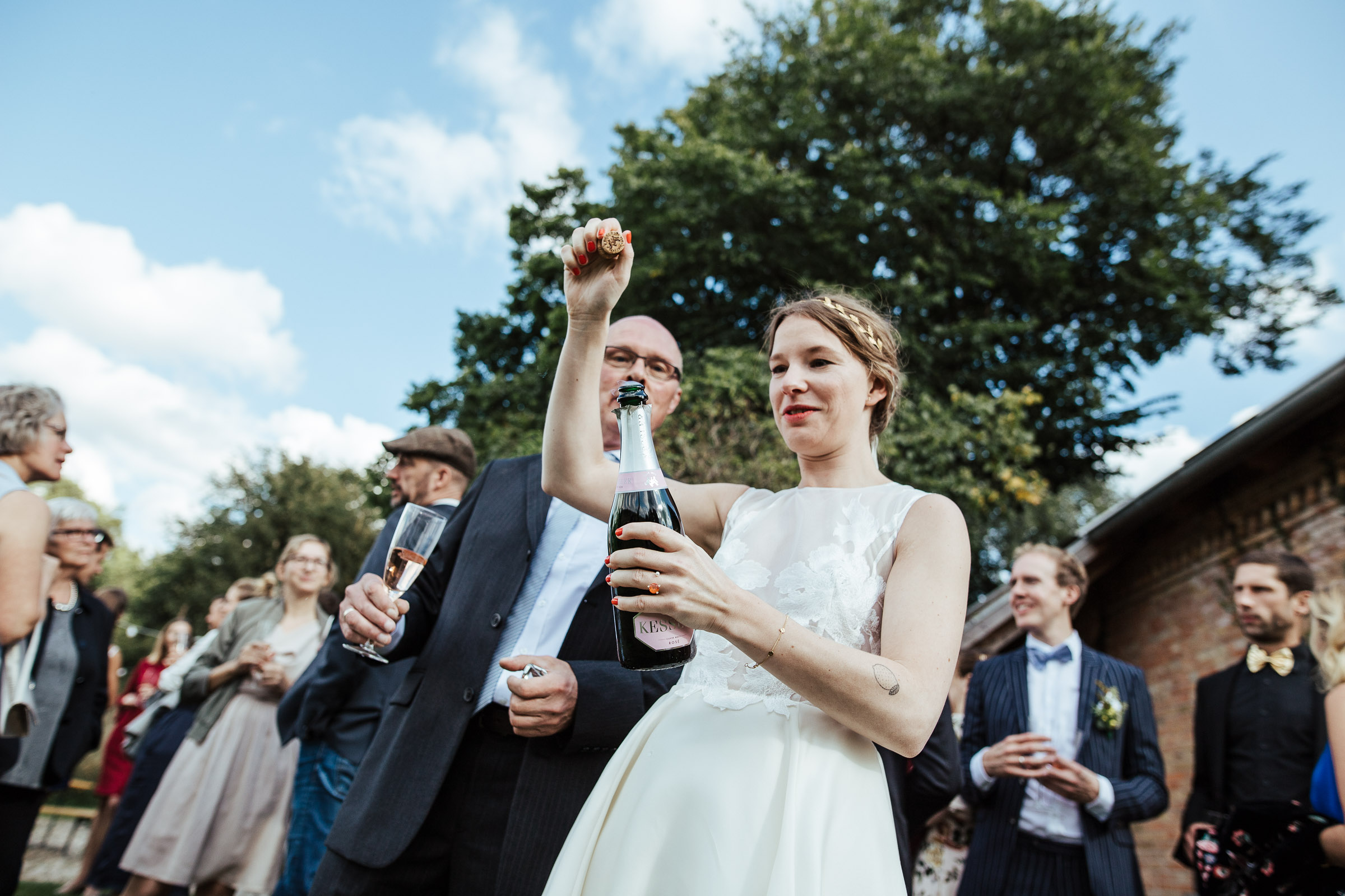 Landhochzeit: Braut öffnet eine Flasche Kessler Sekt