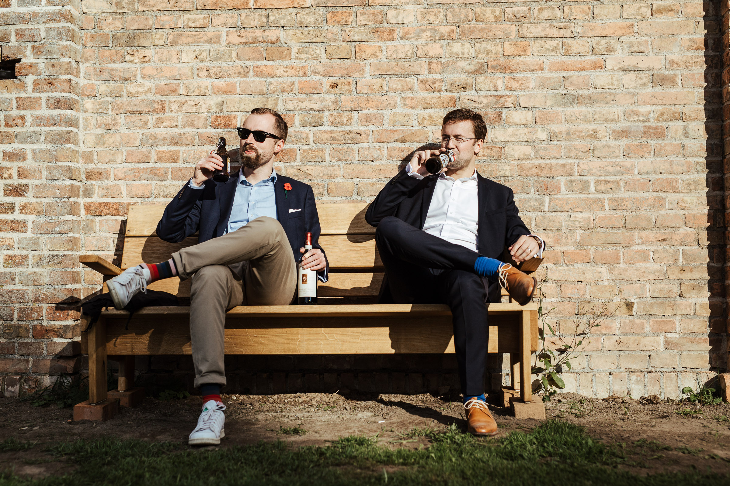 Landhochzeit: zwei Hochzeitsgäste trinken Bier auf einer Bank im Sonnenschein
