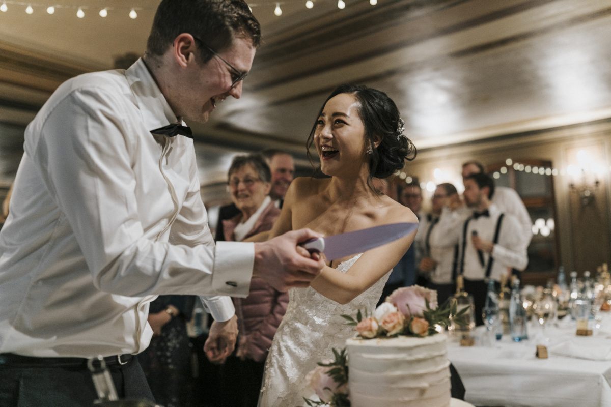 Hochzeitsfotograf in Augsburg: lachendes Brautpaar schneidet Hochzeitstorte an