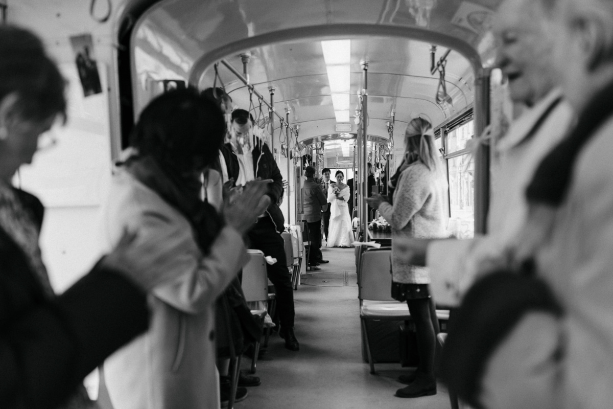 Hochzeitsfotograf in Augsburg: Hochzeitsgäste begrüßen klatschend das Brautpaar in der Straßenbahn